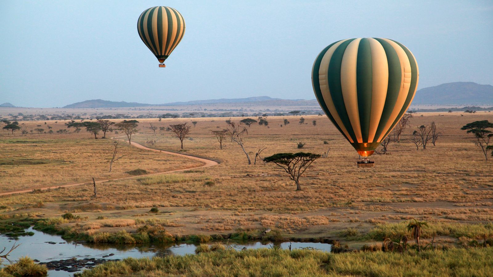 Two hot air balloons drifting low over the Serengeti plains at sunrise