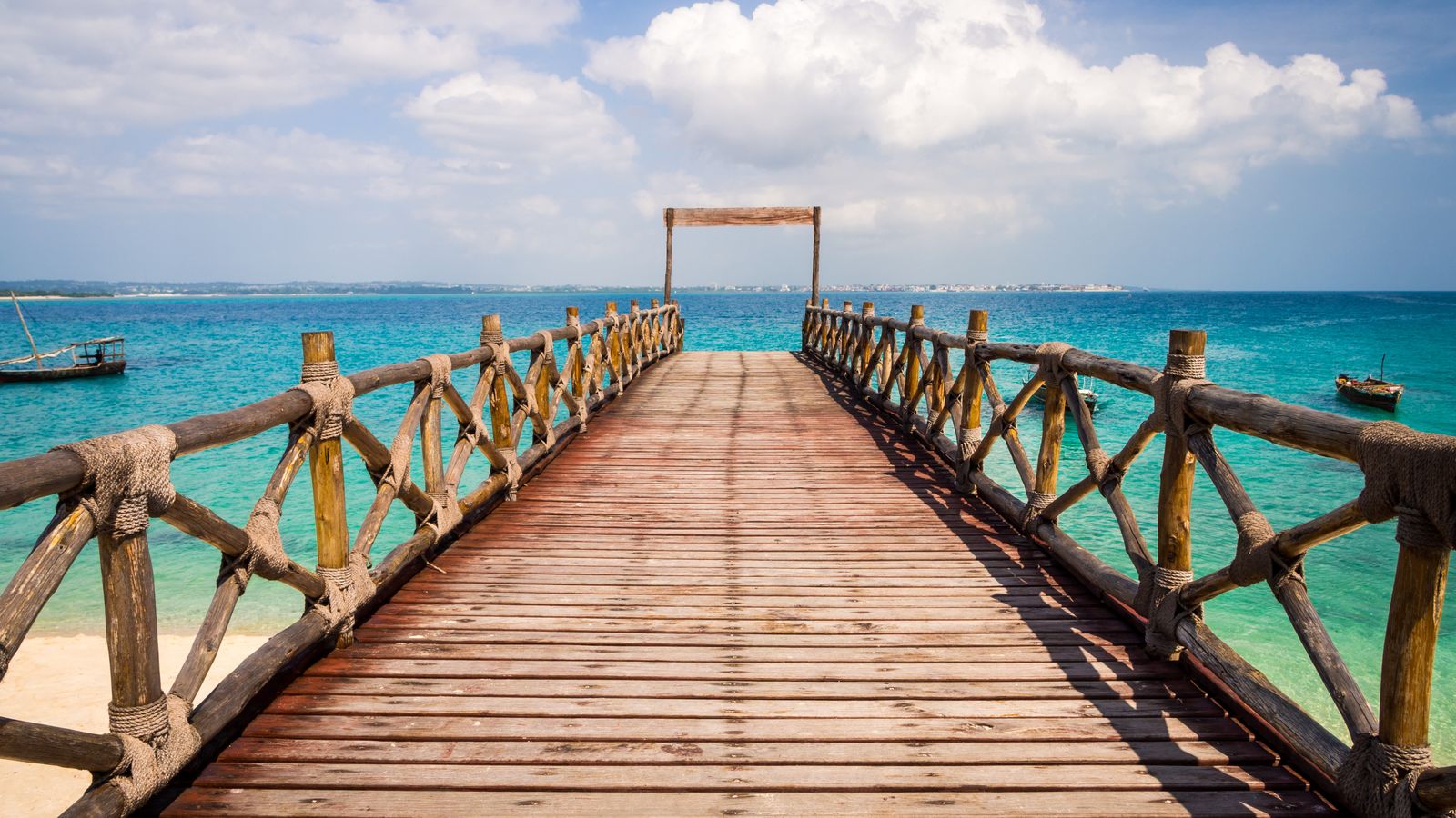 A wooden jetty reaching out over clear turquoise water on the Zanzibar coast